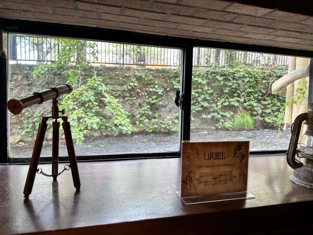 白川の緑が見える窓辺に置かれた望遠鏡とランタン