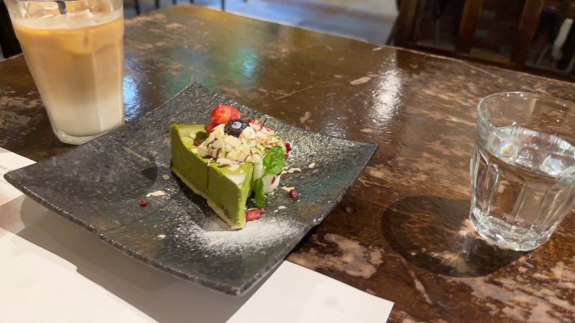 黒い角皿に乗った抹茶のチーズケーキと、カフェラテ