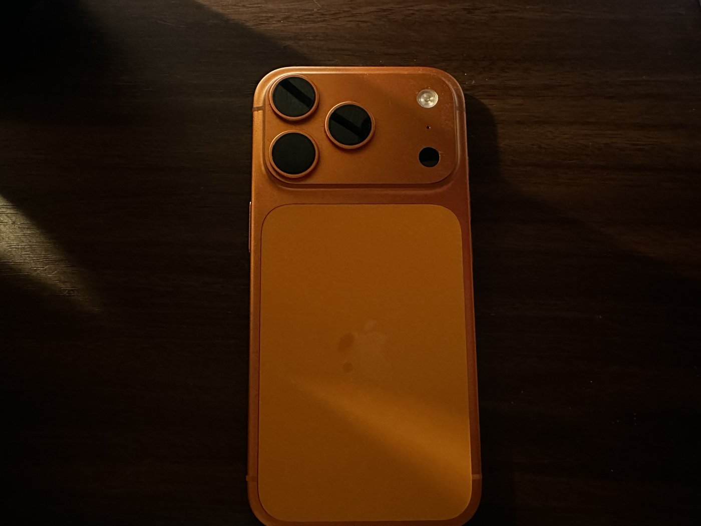 コズミックオレンジのiPhone 17 Proの背面。三眼カメラと、上下で色味が分かれる境目