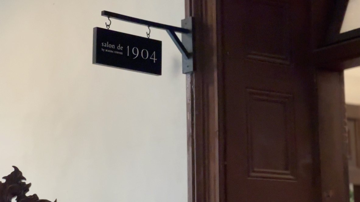 木の扉の横に吊られた黒い看板「salon de 1904 by MAEDA COFFEE」