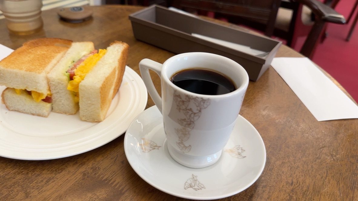 木のテーブルに玉子サンドの皿と、白いカップに入ったコーヒー